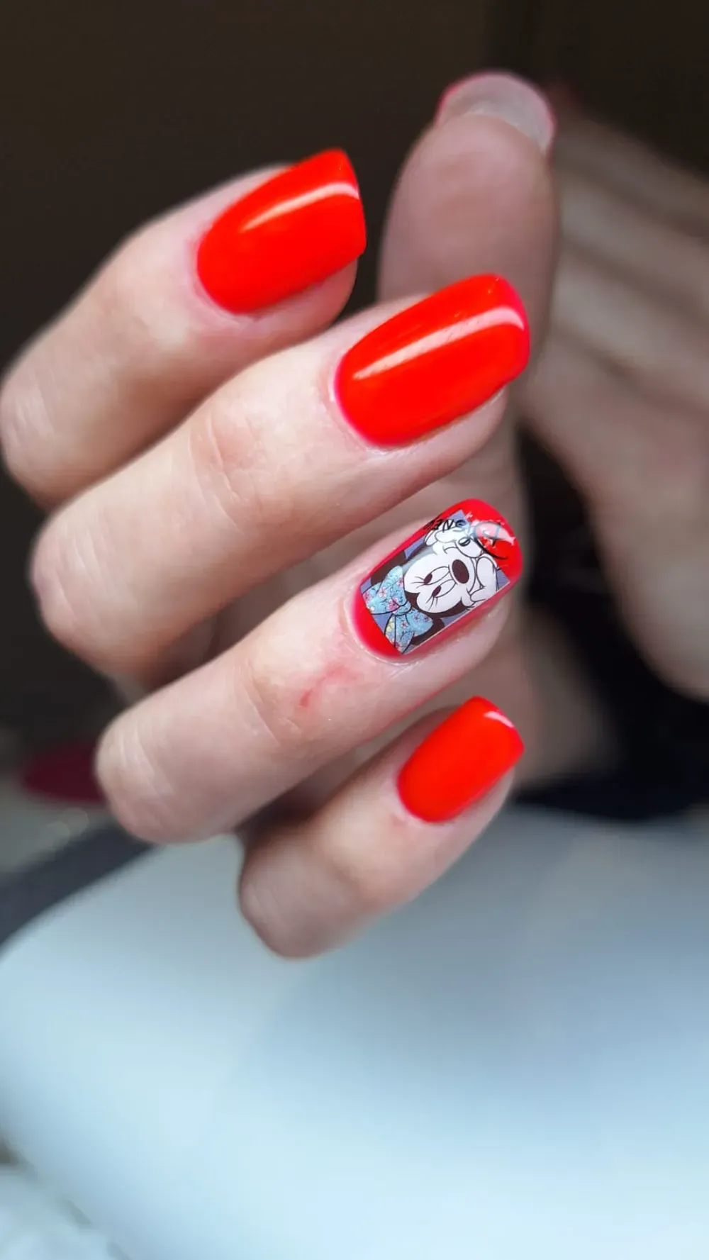 Uñas ovaladas de color rojo con una uña acentuada que presenta un diseño de calavera y flores.