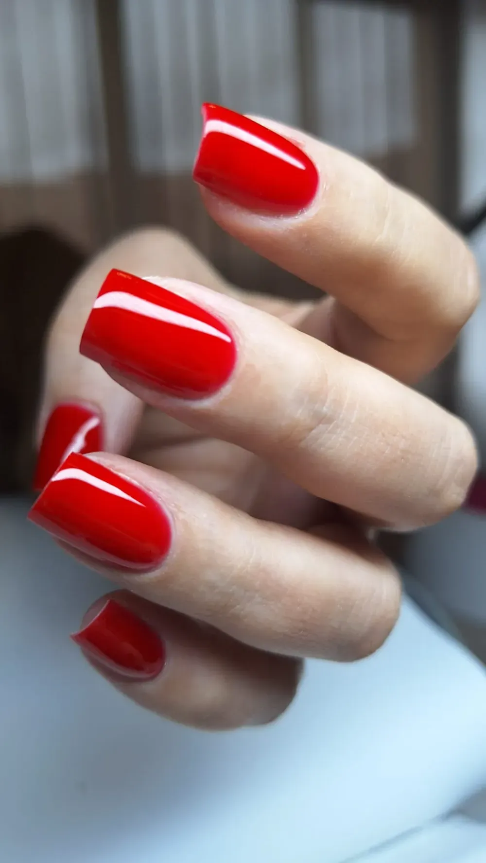 Primer plano de una mano con esmalte de uñas rojo brillante y de forma cuadrada.