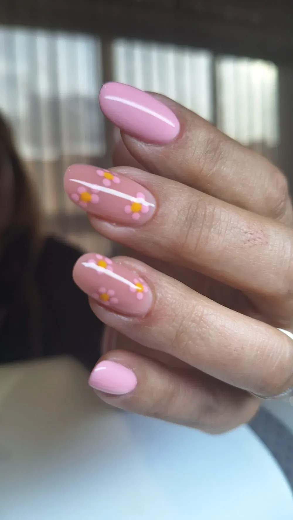 Mano con uñas ovaladas de color rosa claro, una de ellas decorada con pequeñas flores amarillas y rosas.