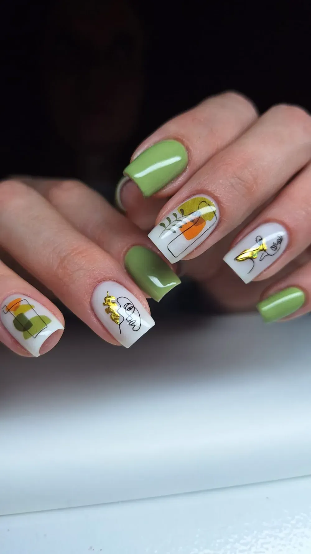 Uñas verdes y blancas con diseños dorados y naranjas.
