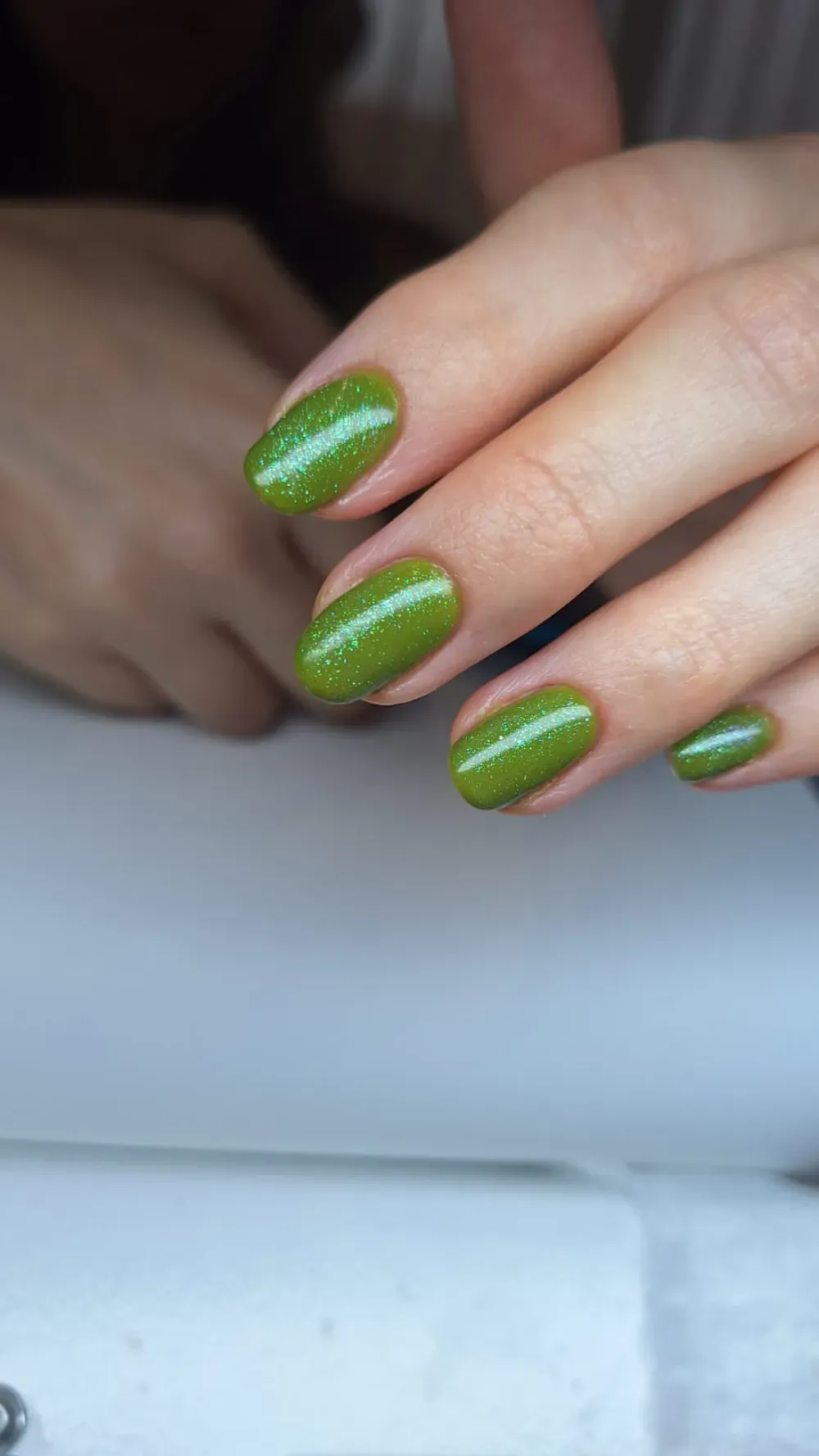 Primer plano de una mano con esmalte de uñas verde brillante de forma ovalada sobre una superficie blanca.