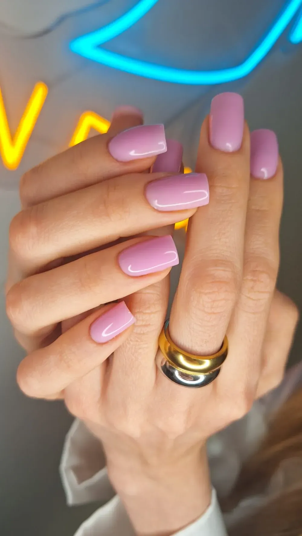 Manos con uñas cuadradas de color violeta claro, luciendo un anillo de oro y plata.