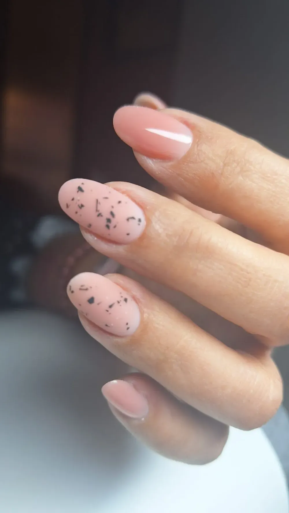 Mano con uñas en forma de almendra; una con motas, el resto de color rosa pálido.