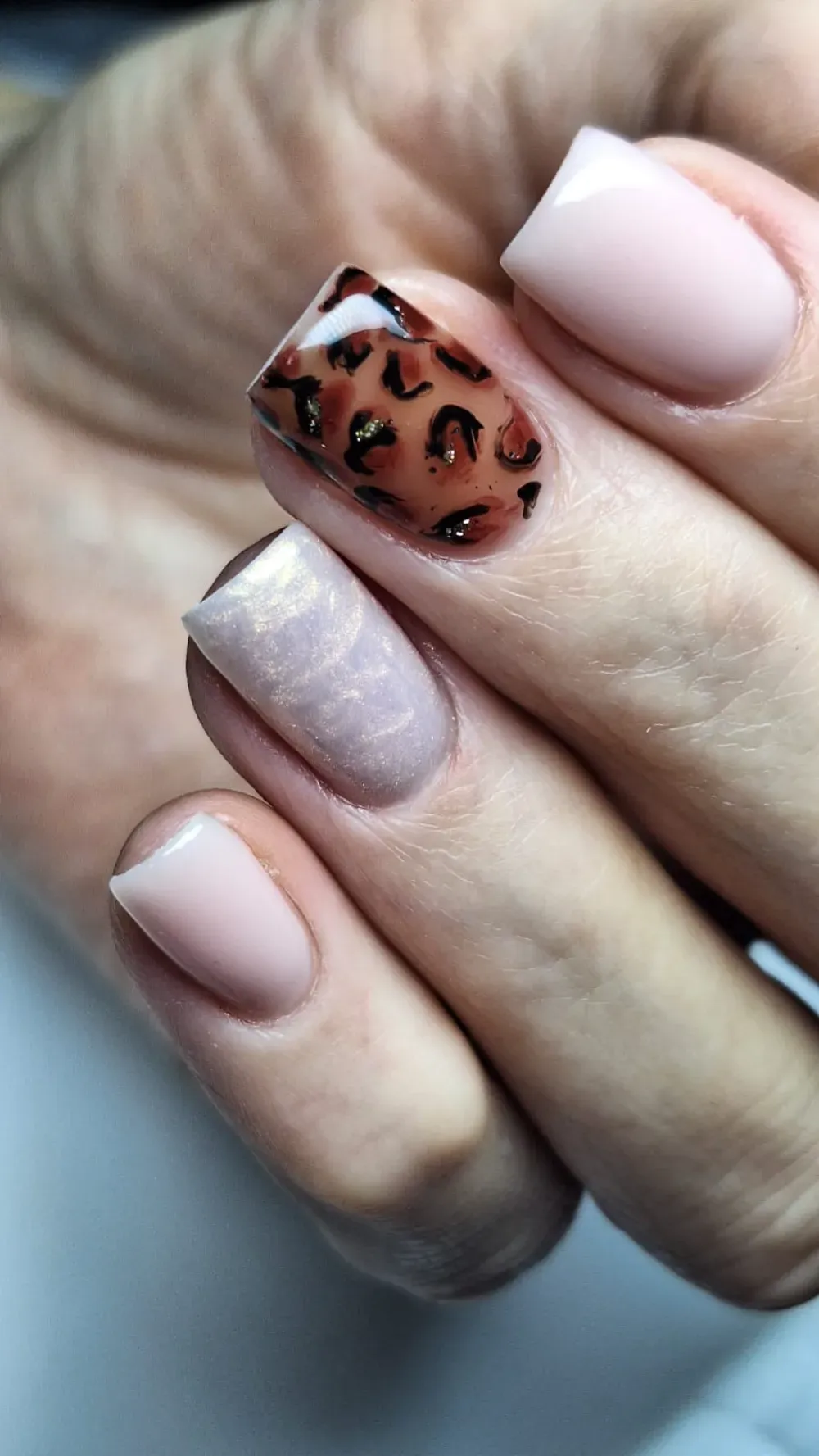 Primer plano de mano con uñas de forma cuadrada; diseños de uñas en tonos beige y con estampado de leopardo.