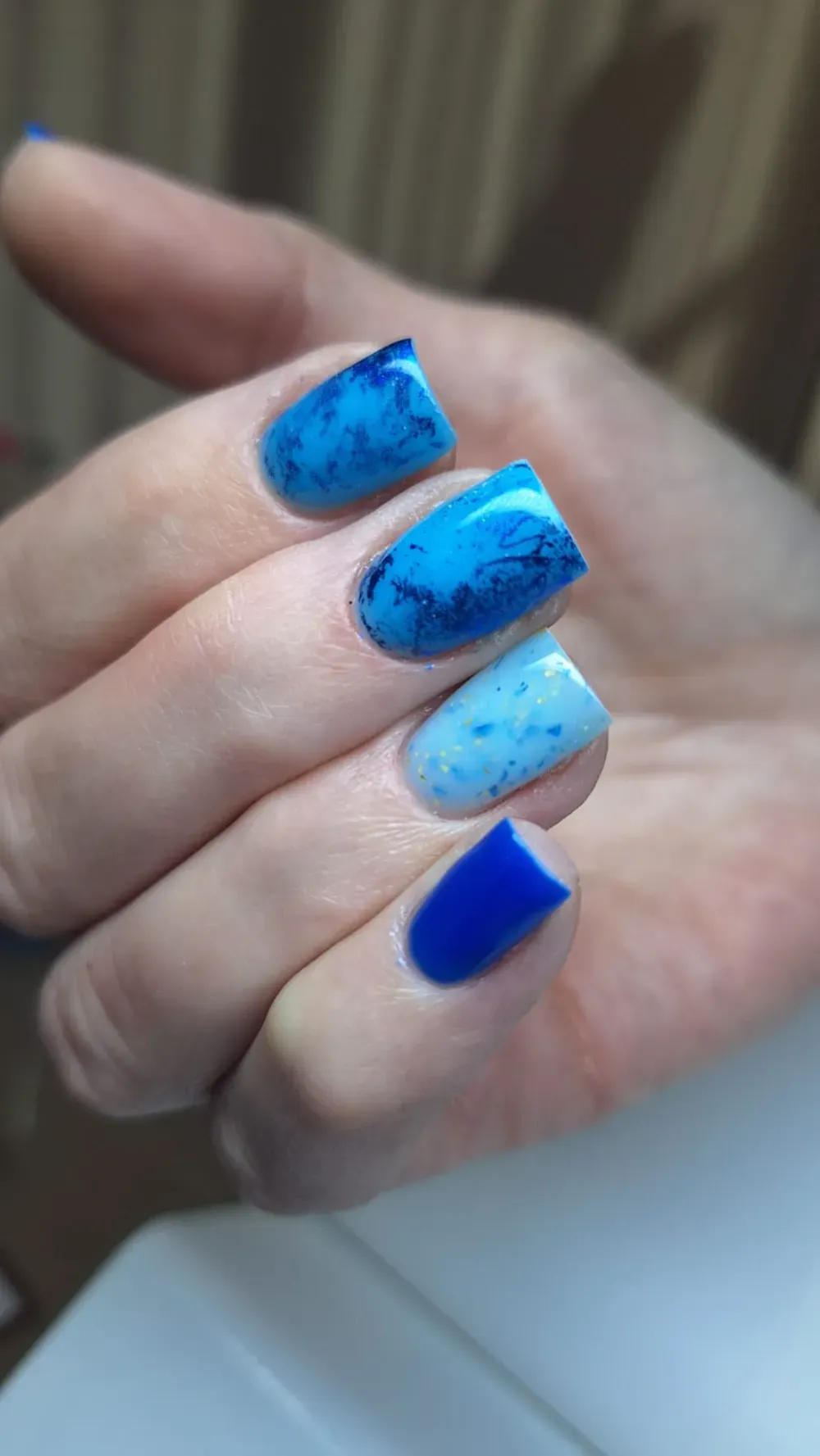 Mano con uñas de forma cuadrada en varios tonos de azul, algunas con efecto mármol.