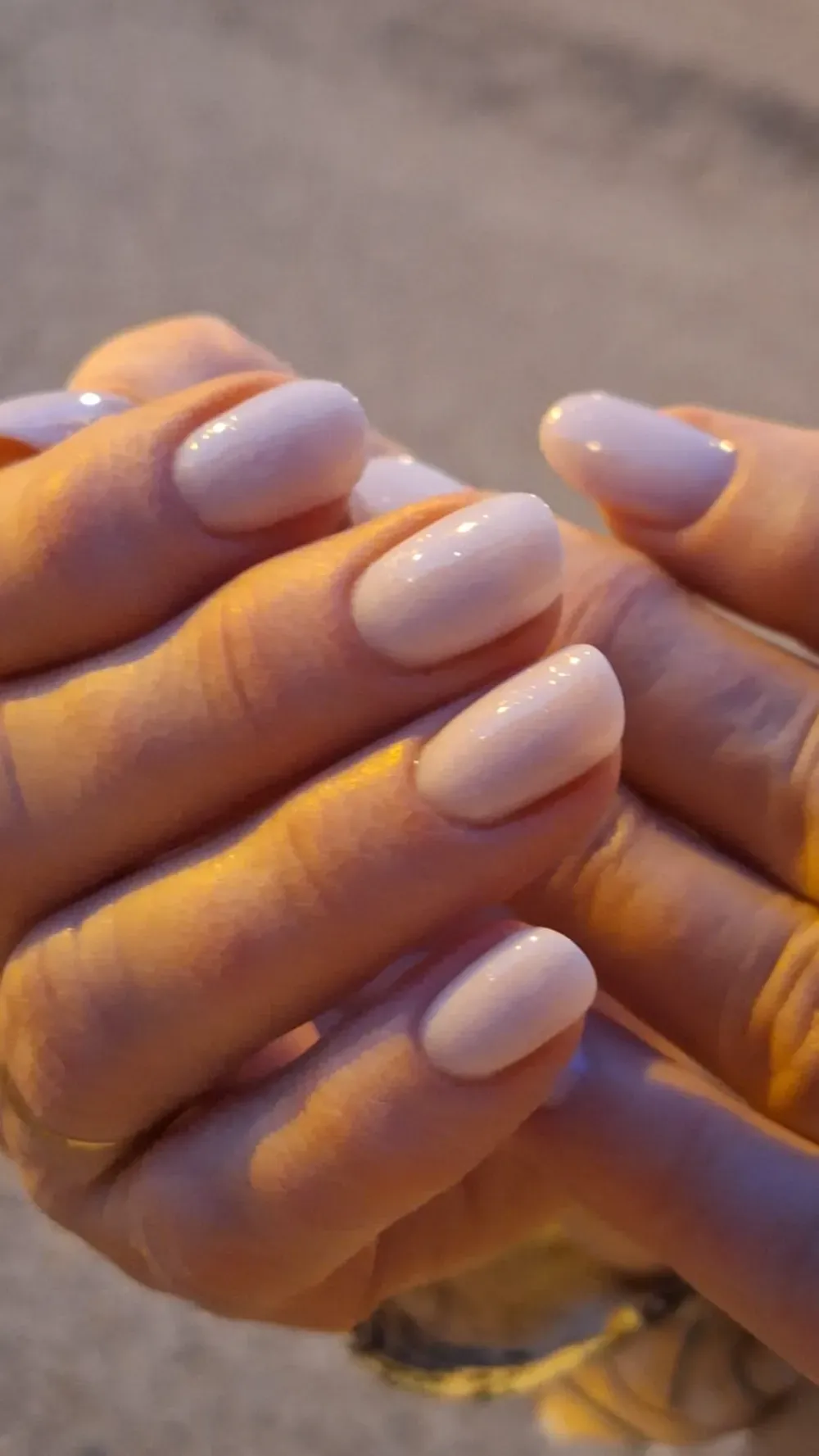 Manos con uñas ovaladas pintadas de rosa claro. Las uñas reflejan la luz, creando un efecto brillante.