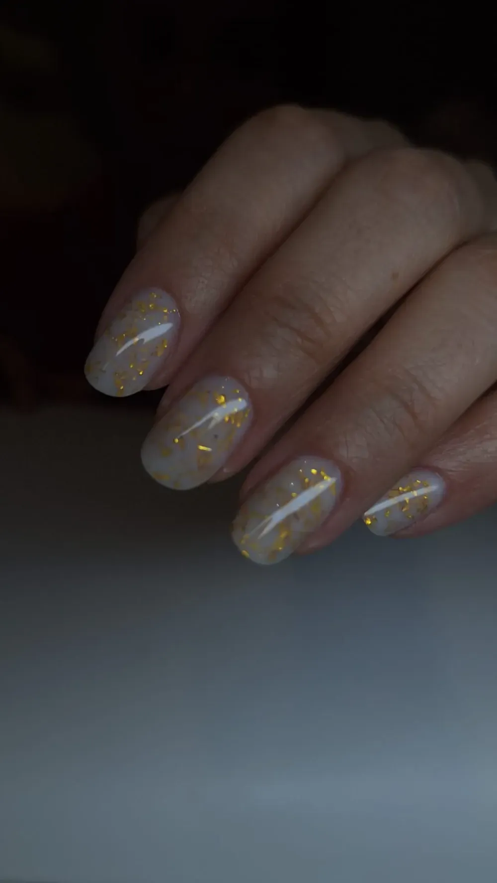 Mano cuidada con uñas de color beige claro y motas doradas.