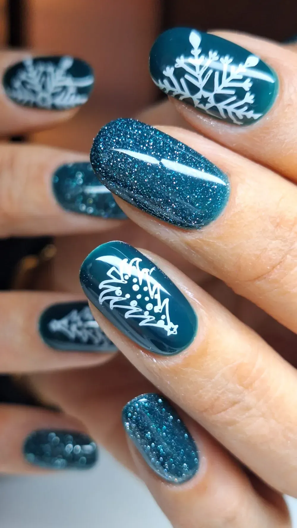 Uñas de gel color verde azulado con diseños de copos de nieve blancos y árboles de Navidad, algunos con brillo.