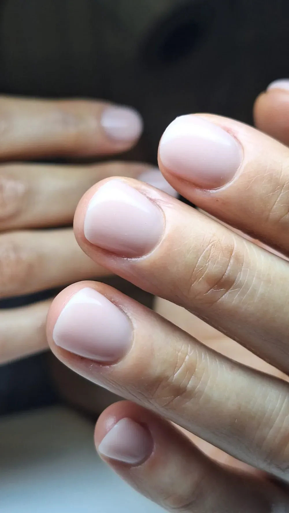 Primer plano de manos con uñas cortas y ovaladas pintadas de un color nude rosa claro.