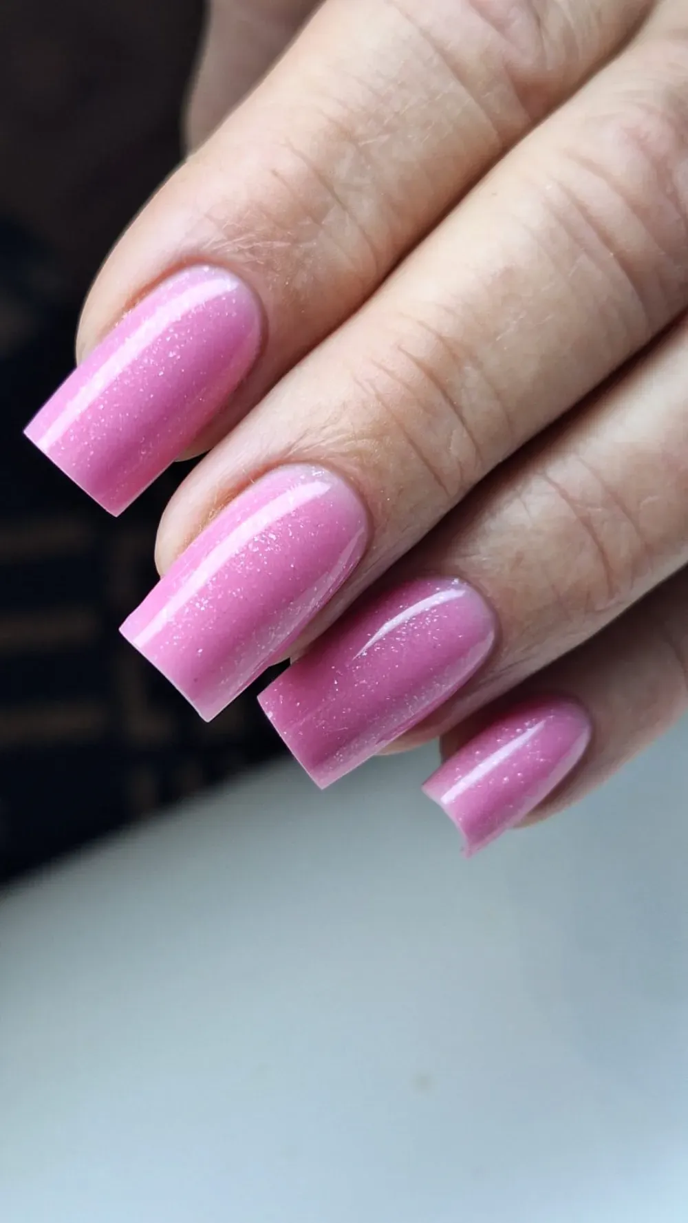 Primer plano de una mano con uñas acrílicas rosas, brillantes y de forma cuadrada.