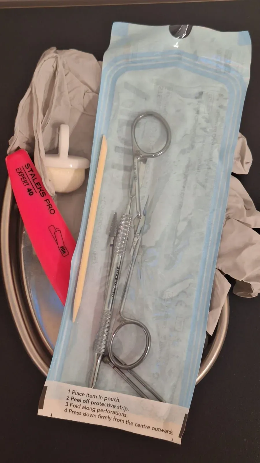 Instrumentos médicos en envases estériles sobre bandeja metálica, que incluyen pinzas, un cepillo.