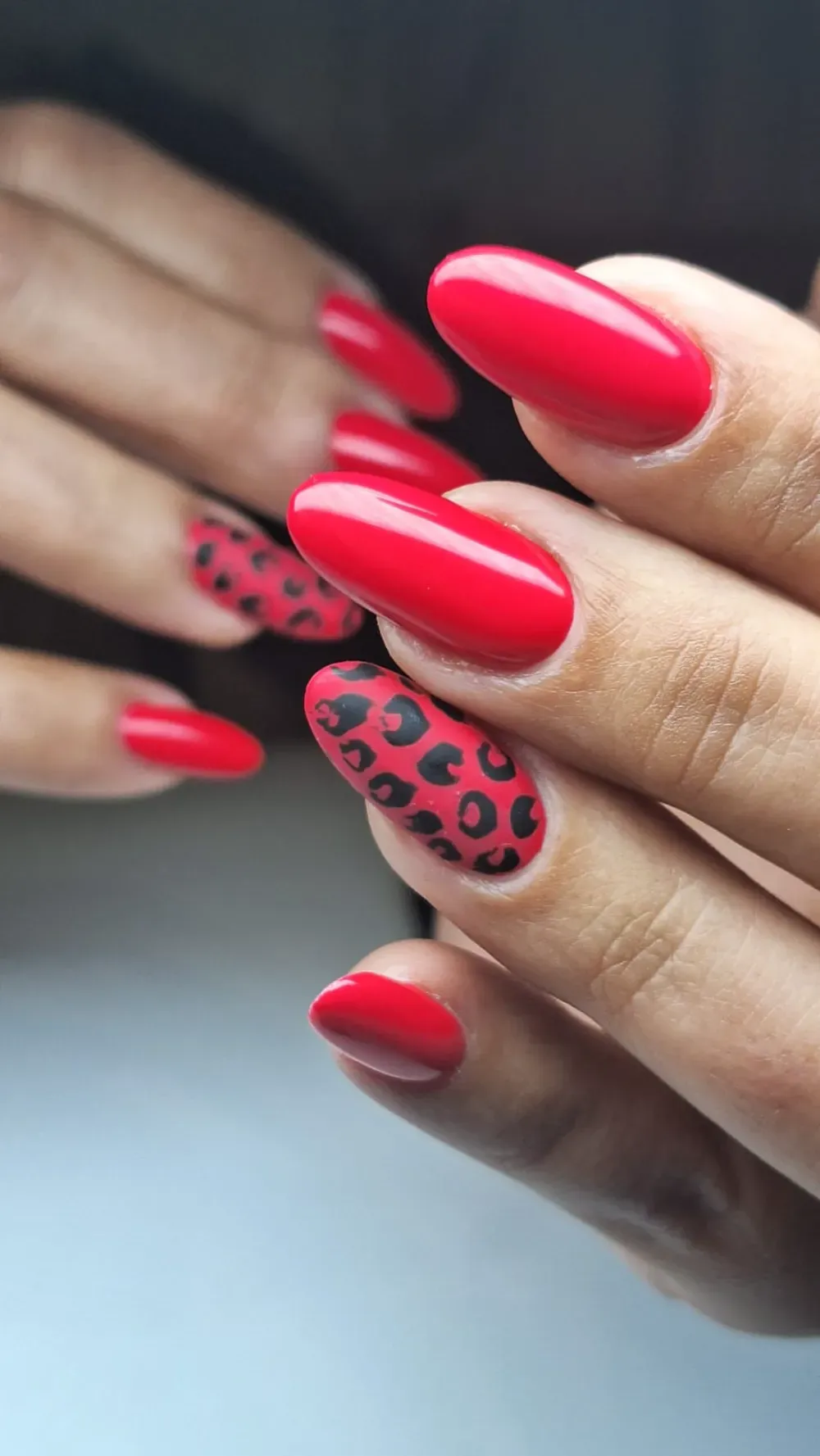 Uñas rojas, cuidadas, de forma ovalada, con detalles de estampado de leopardo en dos uñas.