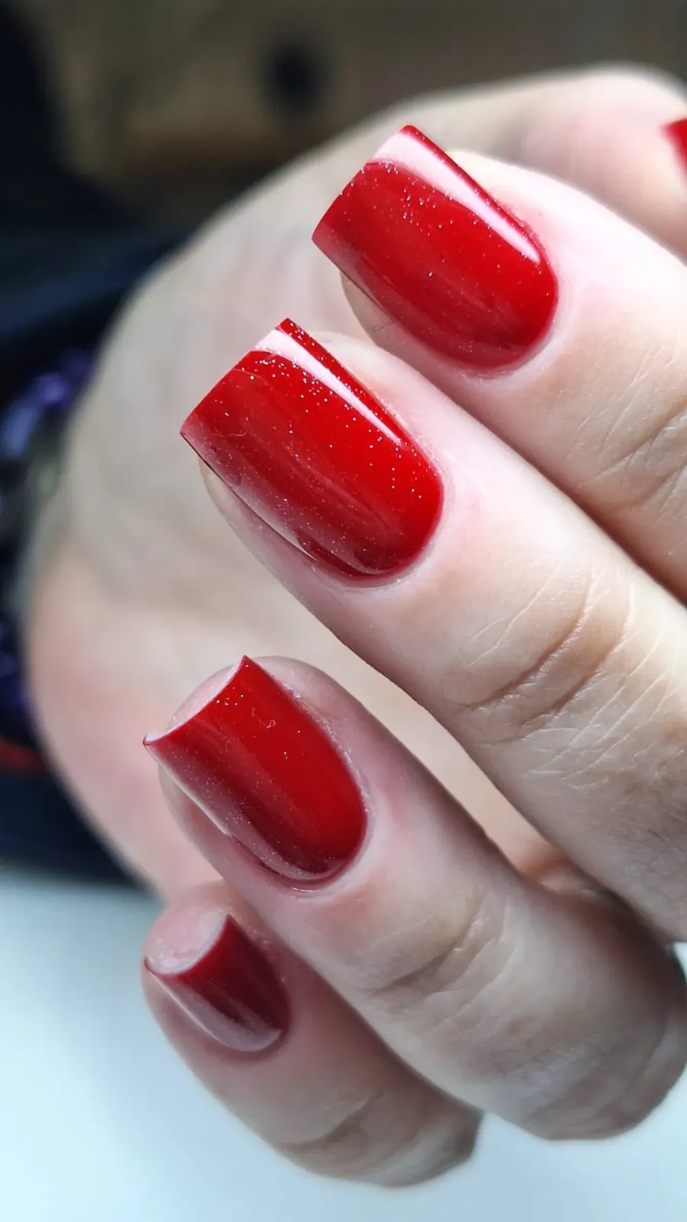 Primer plano de una mano con uñas cuadradas pintadas de un rojo brillante y reluciente.