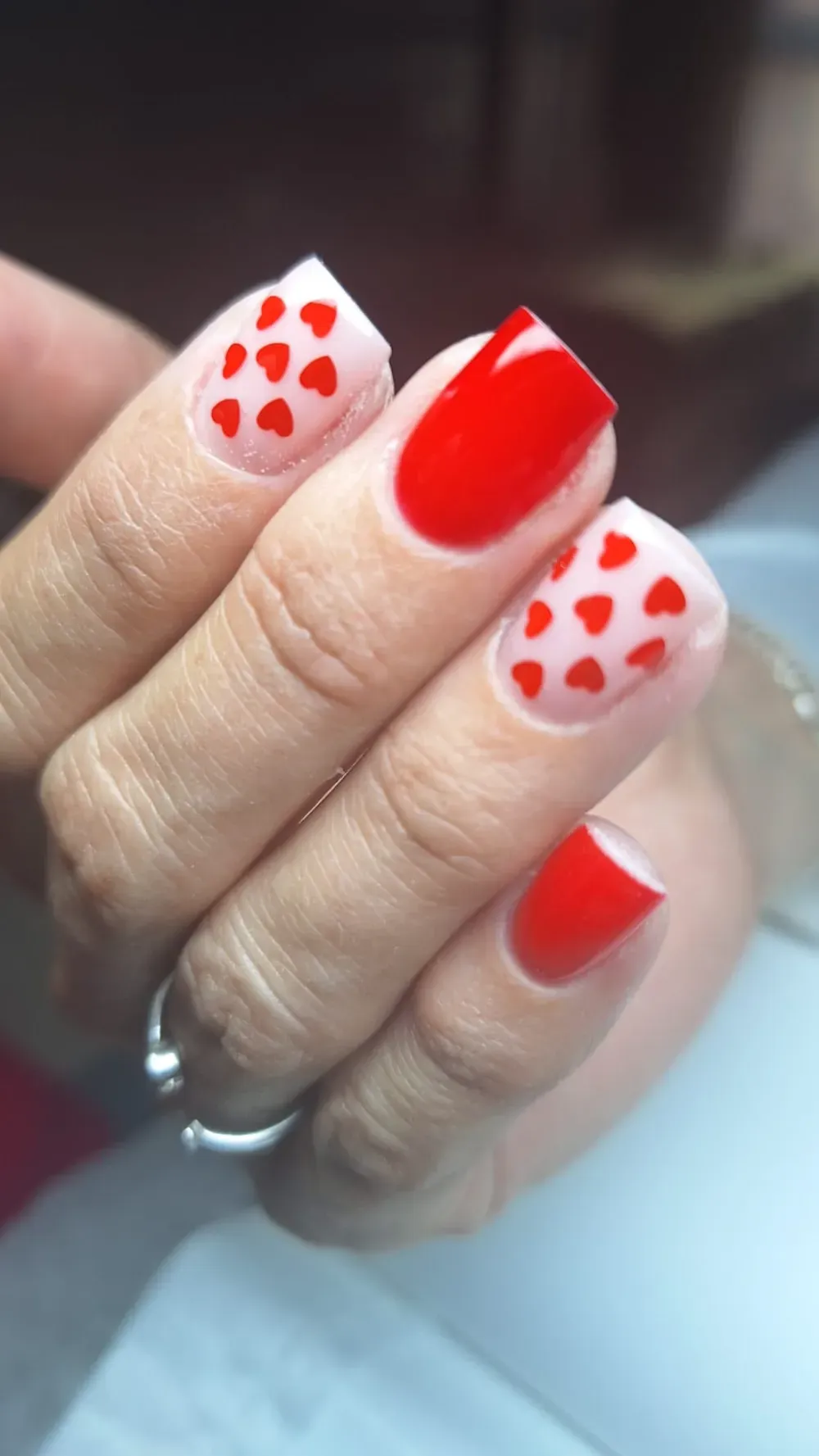 Mano con uñas de color rojo y con dibujos de corazones, sobre fondo blanco.