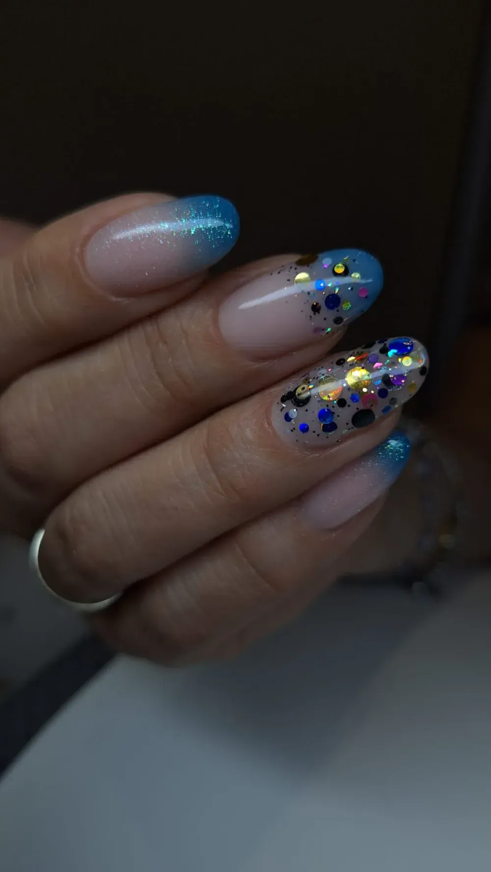 Una mano con uñas largas y ovaladas. Puntas francesas con purpurina azul y diseños con purpurina en algunas uñas.