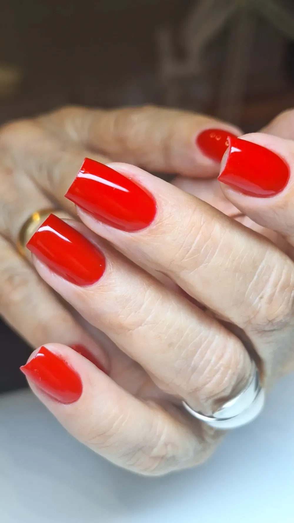 Mano con uñas cuidadas, rojas y de forma cuadrada, anillo de plata.