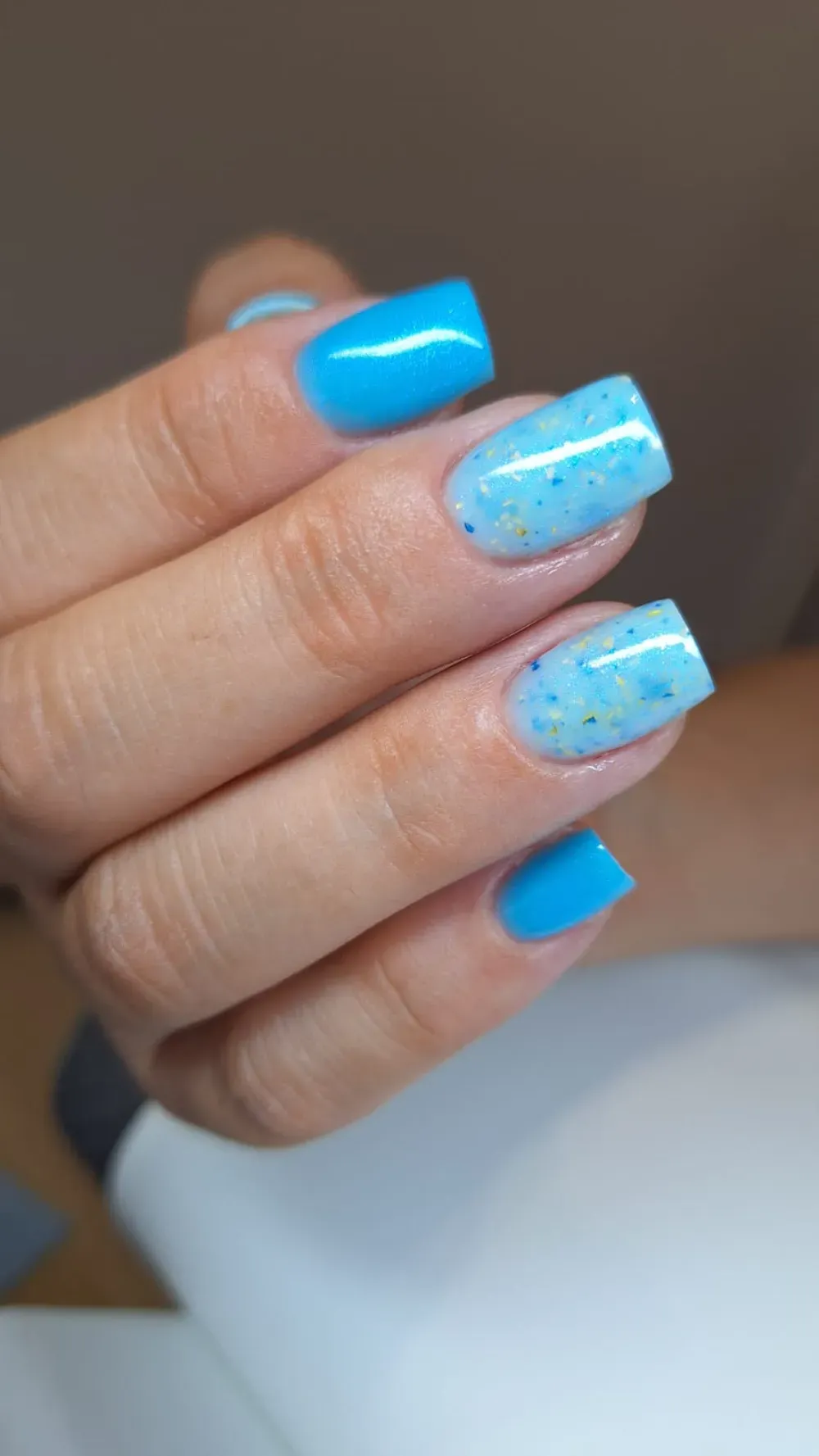 Mano con uñas de forma cuadrada en esmalte azul brillante y azul claro moteado.