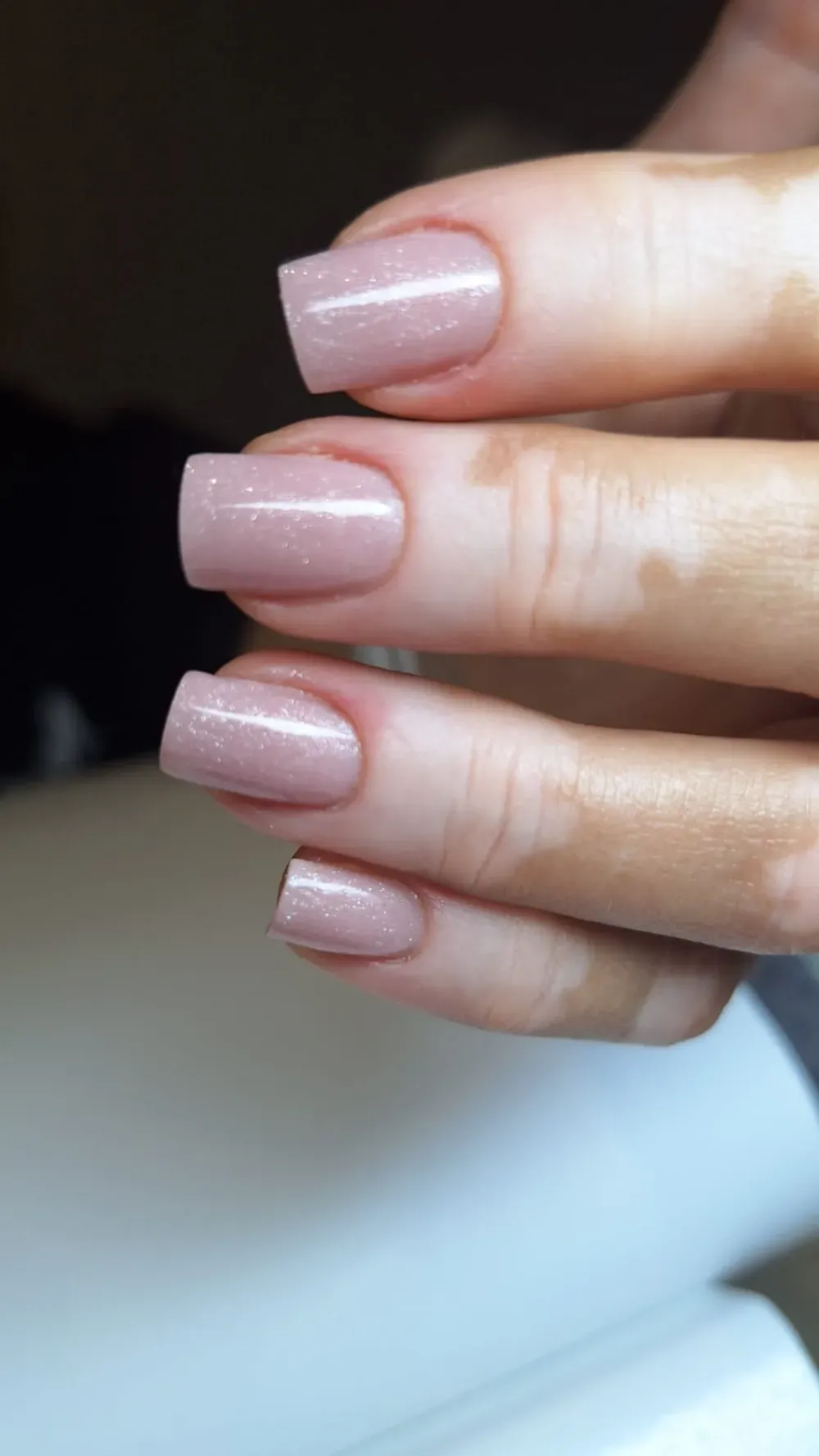 Unas uñas cuadradas pintadas con un esmalte malva claro y brillante se muestran sobre un fondo de piel.