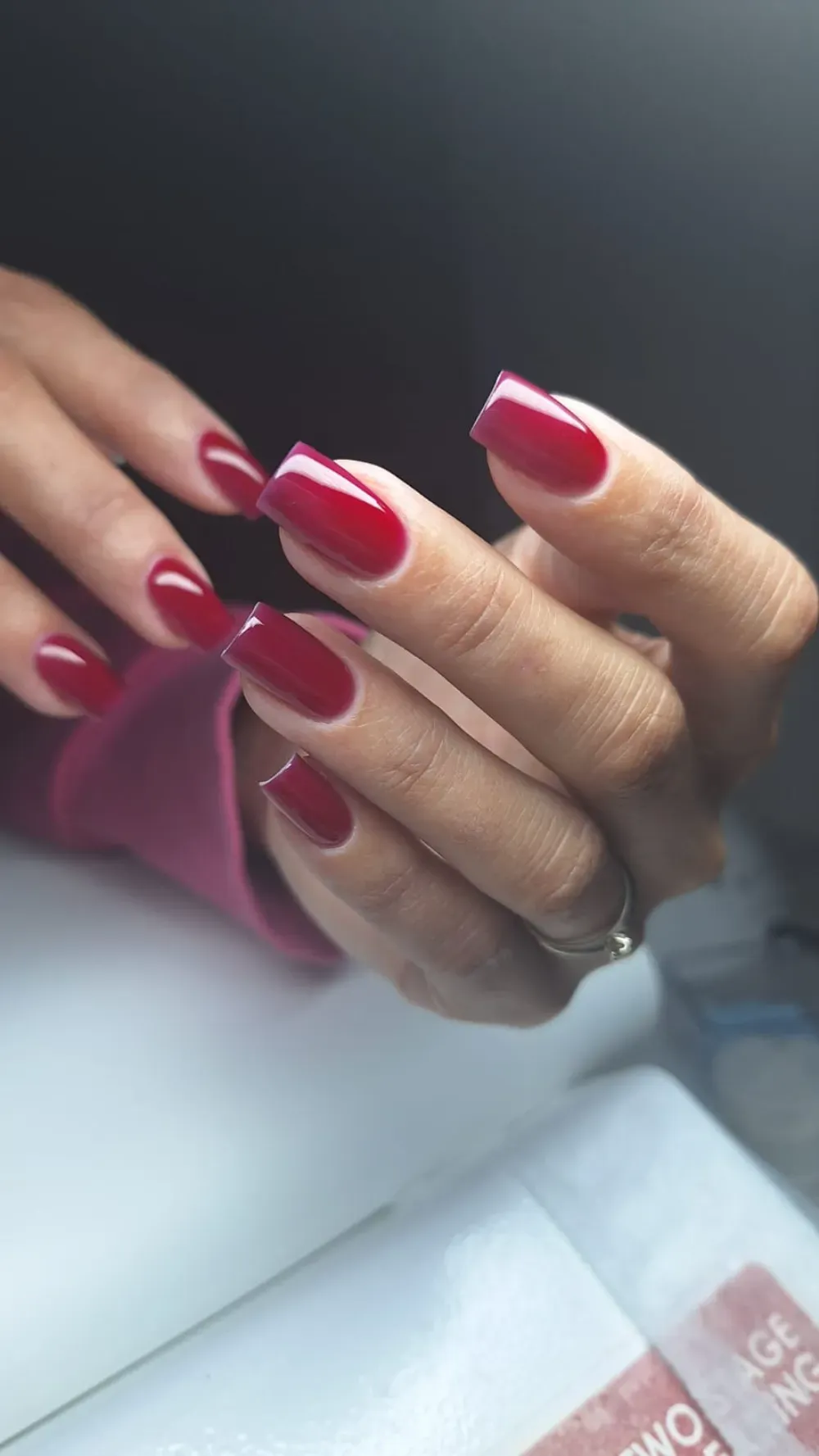 Manos con uñas largas y cuadradas pintadas de un rojo intenso, apoyadas sobre una superficie blanca.