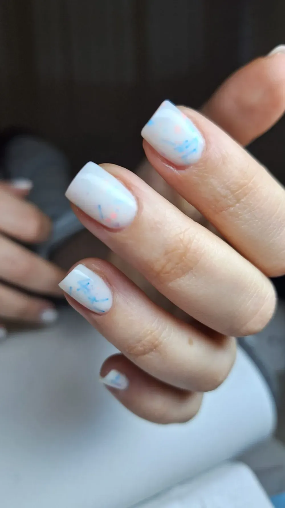 Primer plano de una mano con uñas cuadradas y blancas, con suaves remolinos de color azul y rosa.