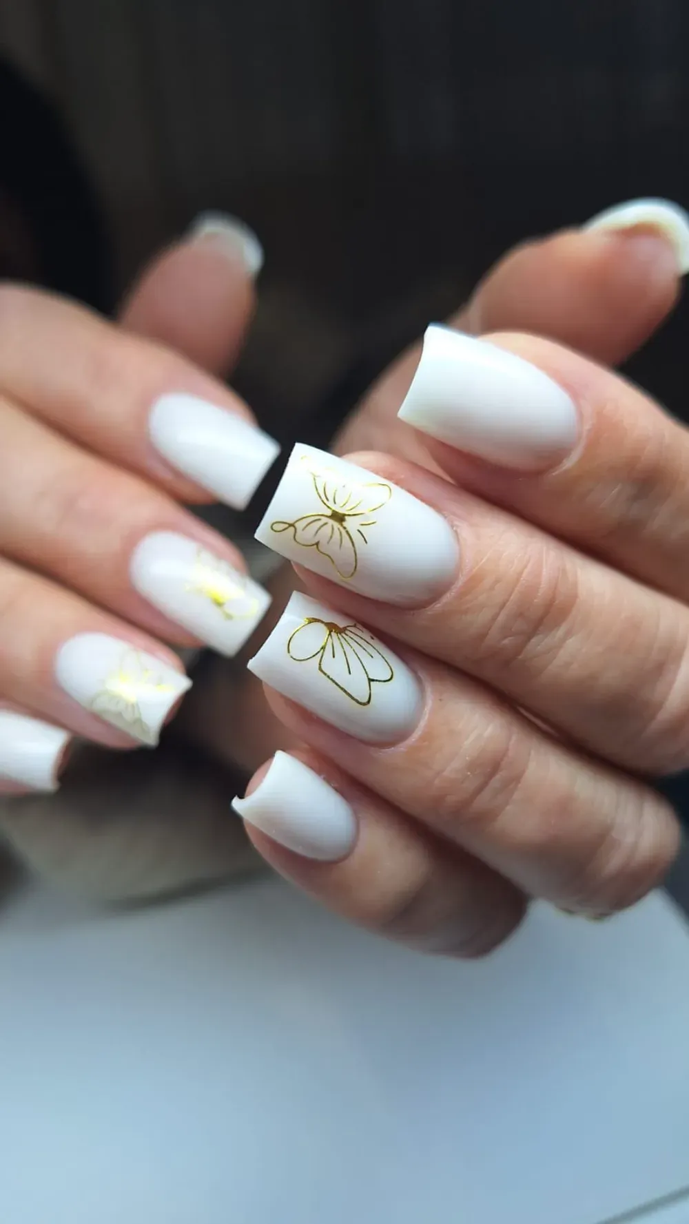 Uñas acrílicas blancas con calcomanías florales doradas.