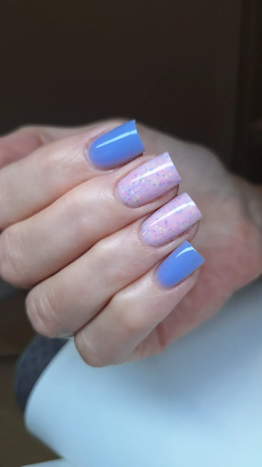 Mano con uñas cuadradas pintadas de azul y rosa brillante.