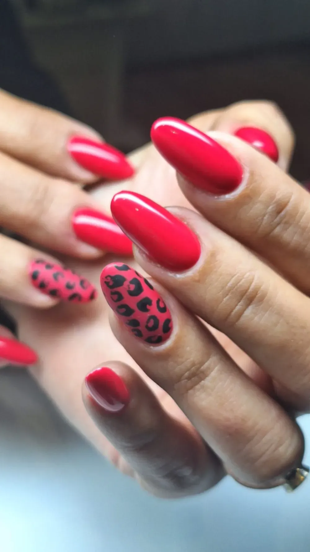 Manos con uñas ovaladas rojas y una con acento de estampado de leopardo.