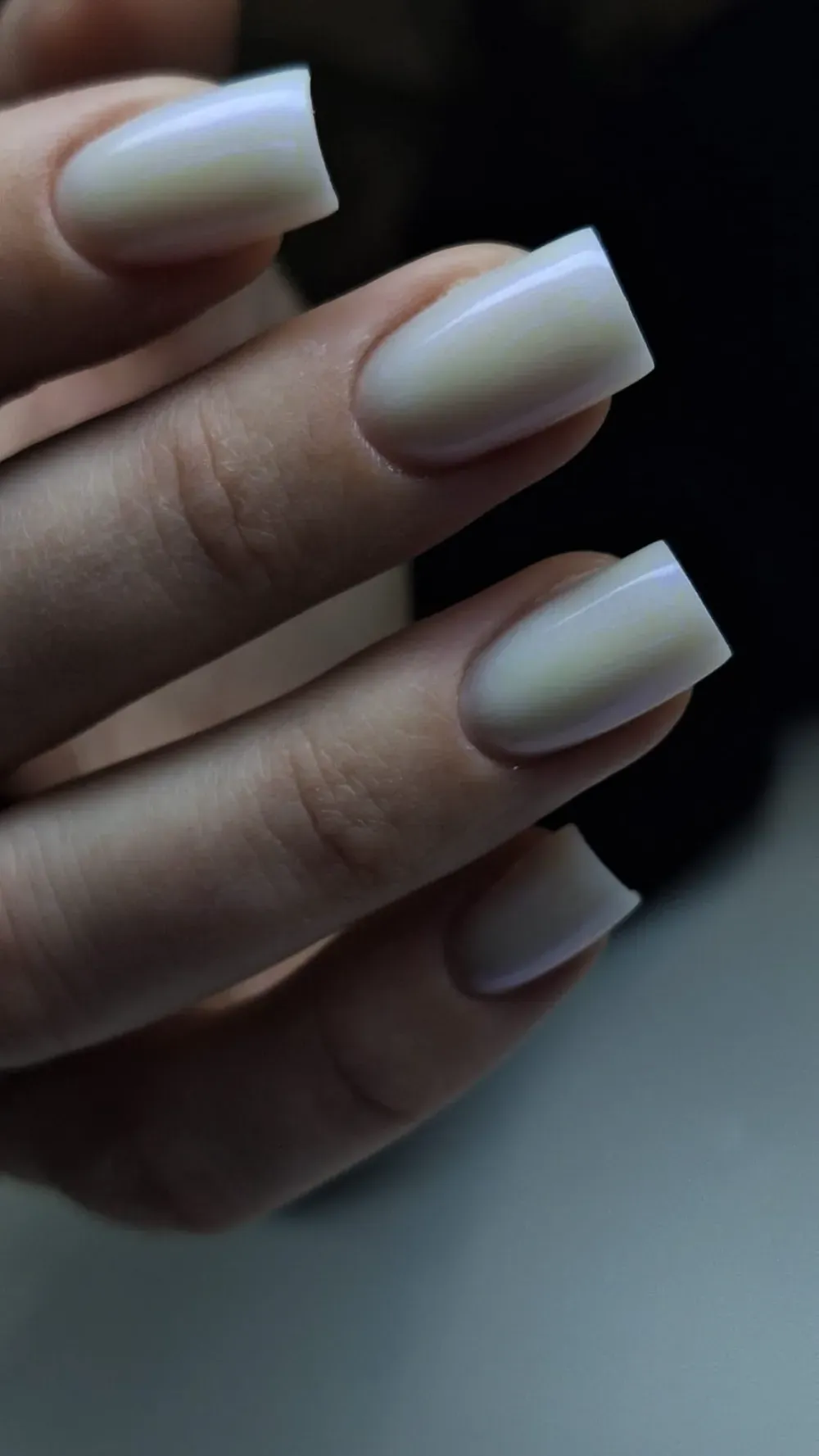 Mano con uñas cuadradas pintadas de un color blanco perlado claro.