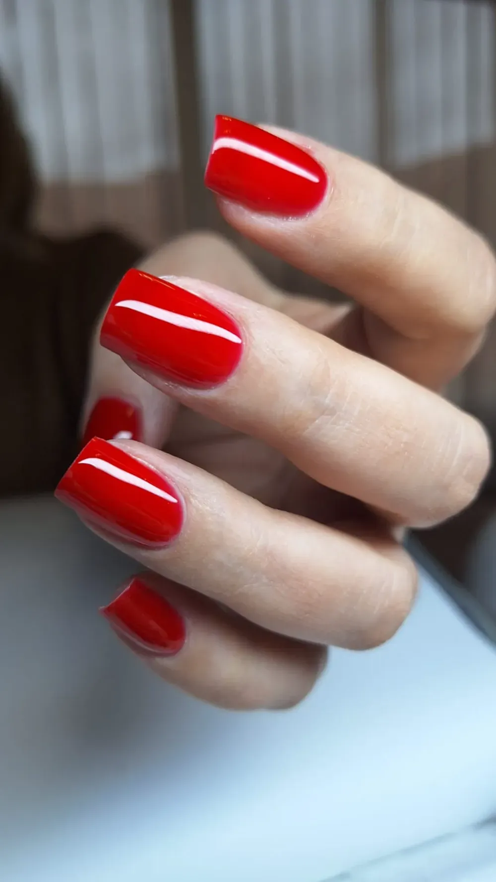 Mano con uñas cuadradas rojas, brillantes y recién pintadas.