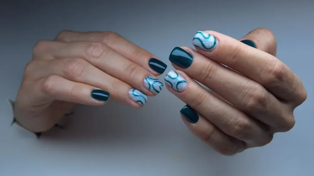 Manos con uñas cortas de color verde azulado oscuro, algunas con diseños en espiral de color azul claro.