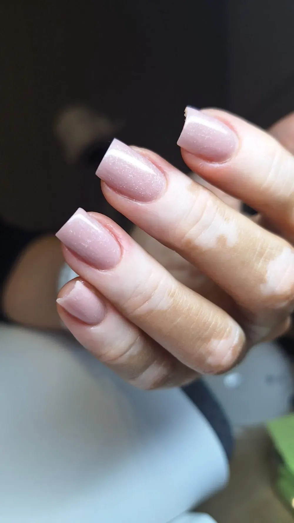 Uñas cuidadas en un tono rosa claro con un sutil brillo. Mano apoyada sobre una superficie.