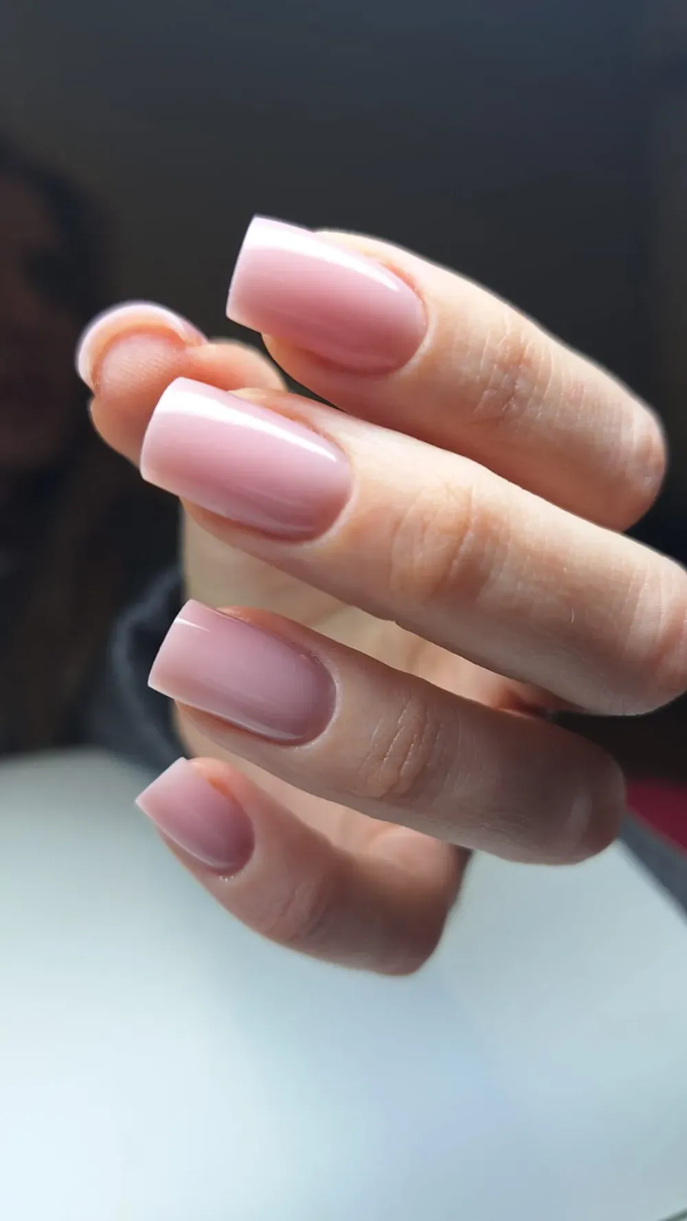 Primer plano de una mano con uñas acrílicas rosas y de forma cuadrada.