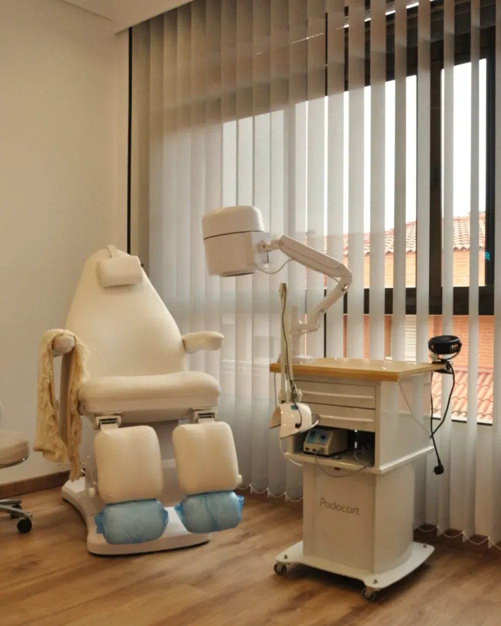 Silla médica con equipo anexo en habitación con ventana y persianas verticales.