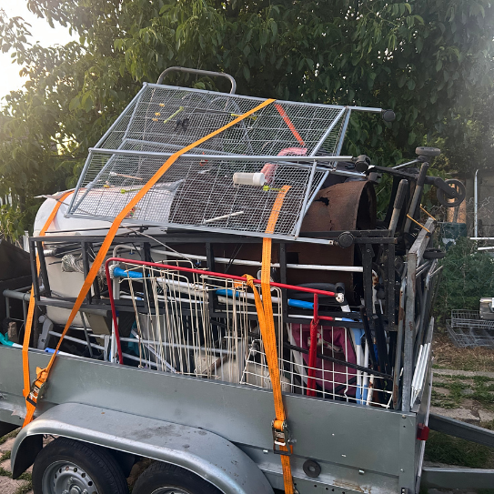 Remorque chargée de ferraille, sécurisée par des sangles orange.