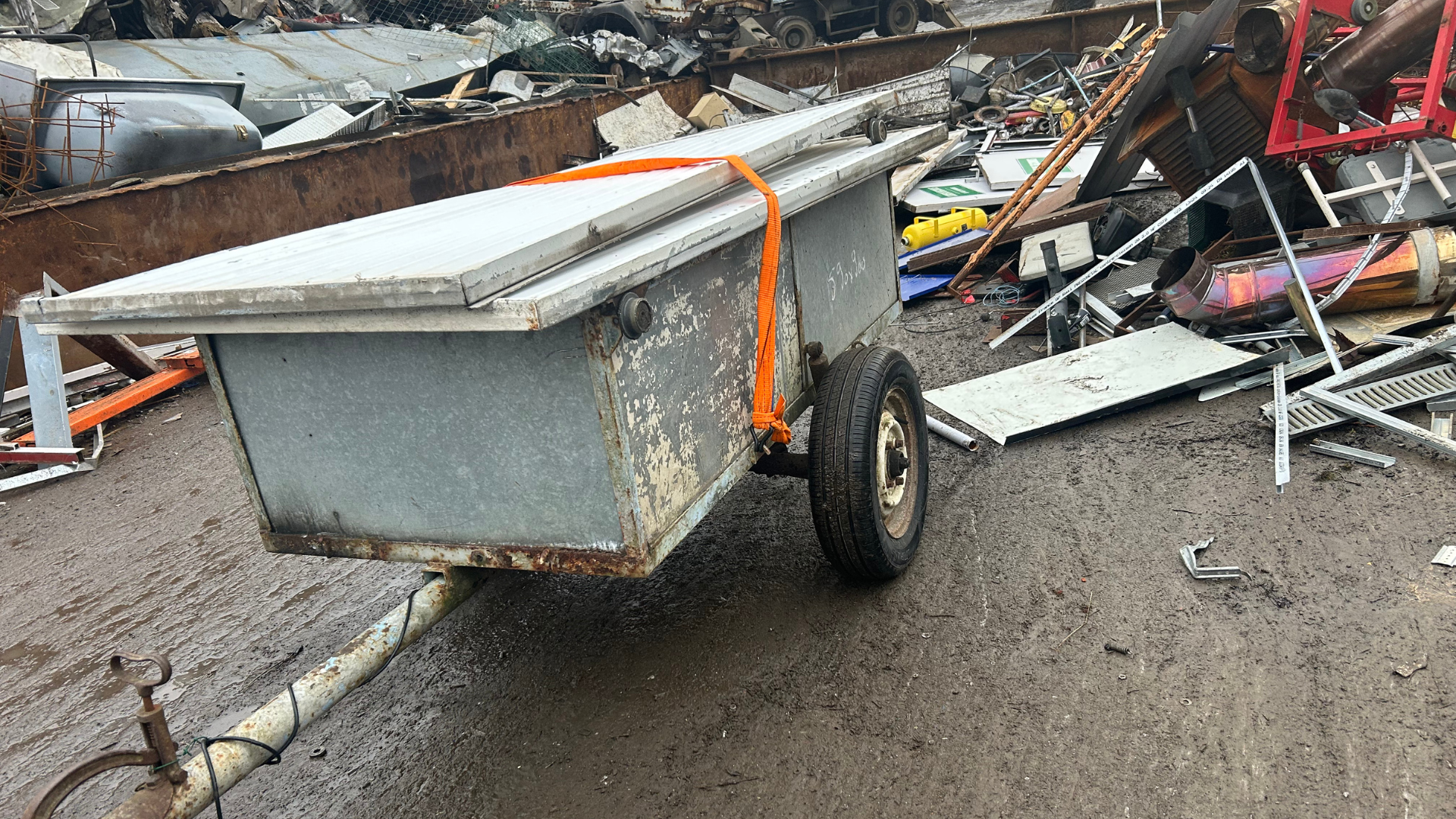 Remorque en métal gris avec sangle orange dans une casse.