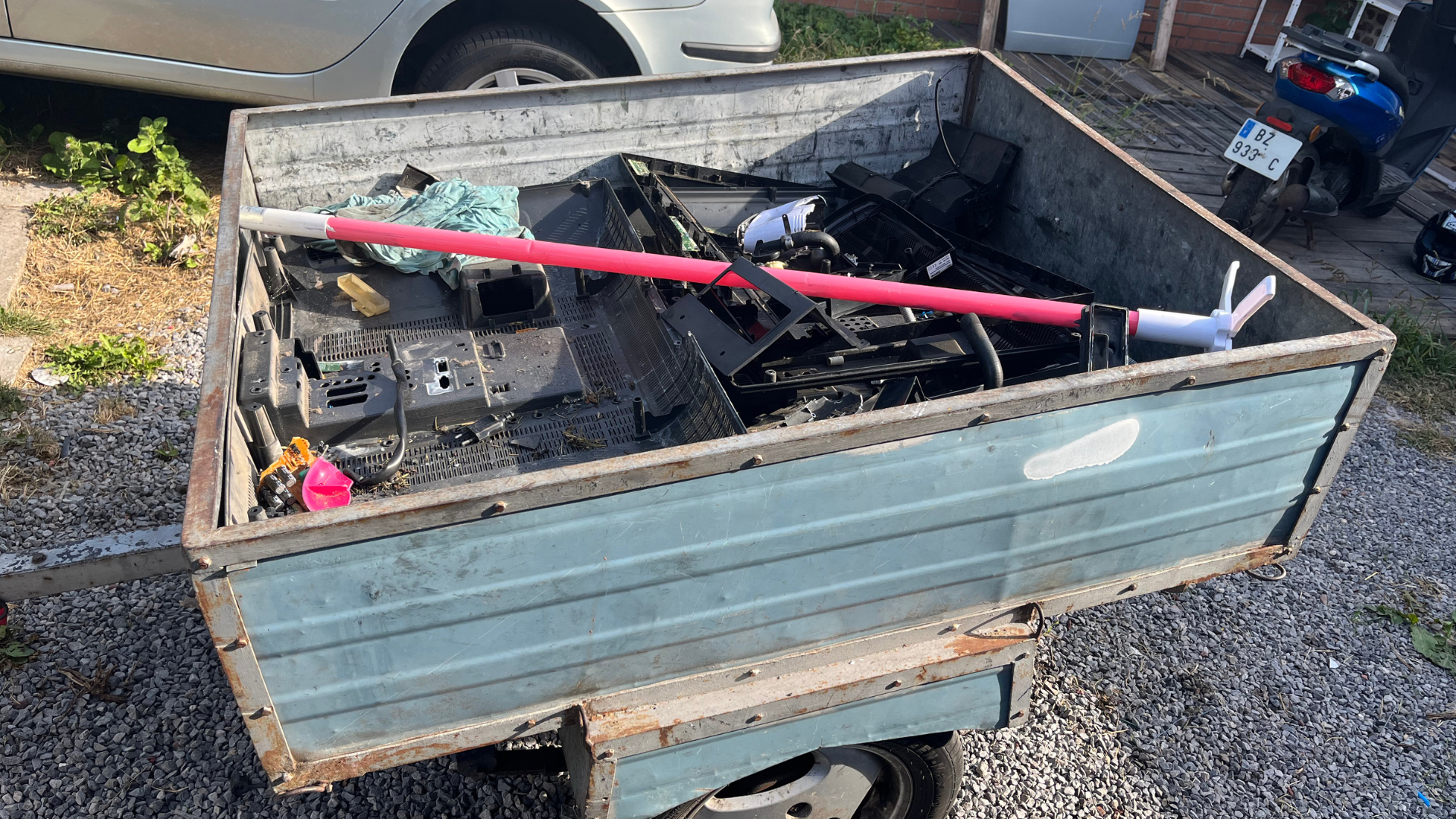 Remorque métallique bleue remplie de ferraille. Poteau rose, moto visible.