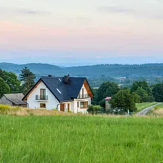 Una casa está situada en medio de un campo de hierba con montañas al fondo.