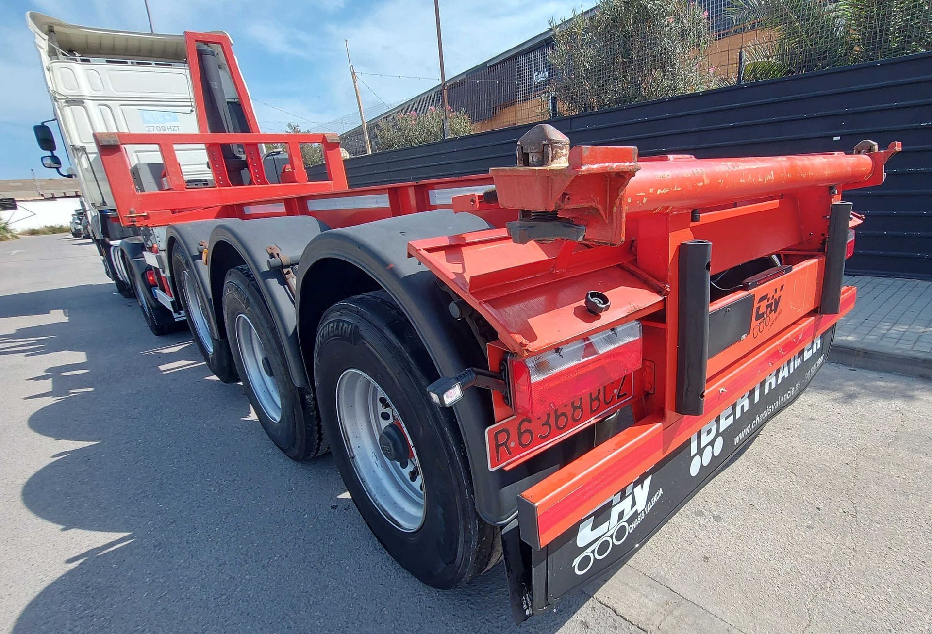 Remolque de camión rojo y negro con cuatro ejes en una carretera asfaltada.
