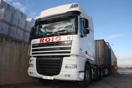 Camión DAF blanco, con el logotipo "ROIG", estacionado cerca de bloques de hormigón y contenedores bajo un cielo azul.