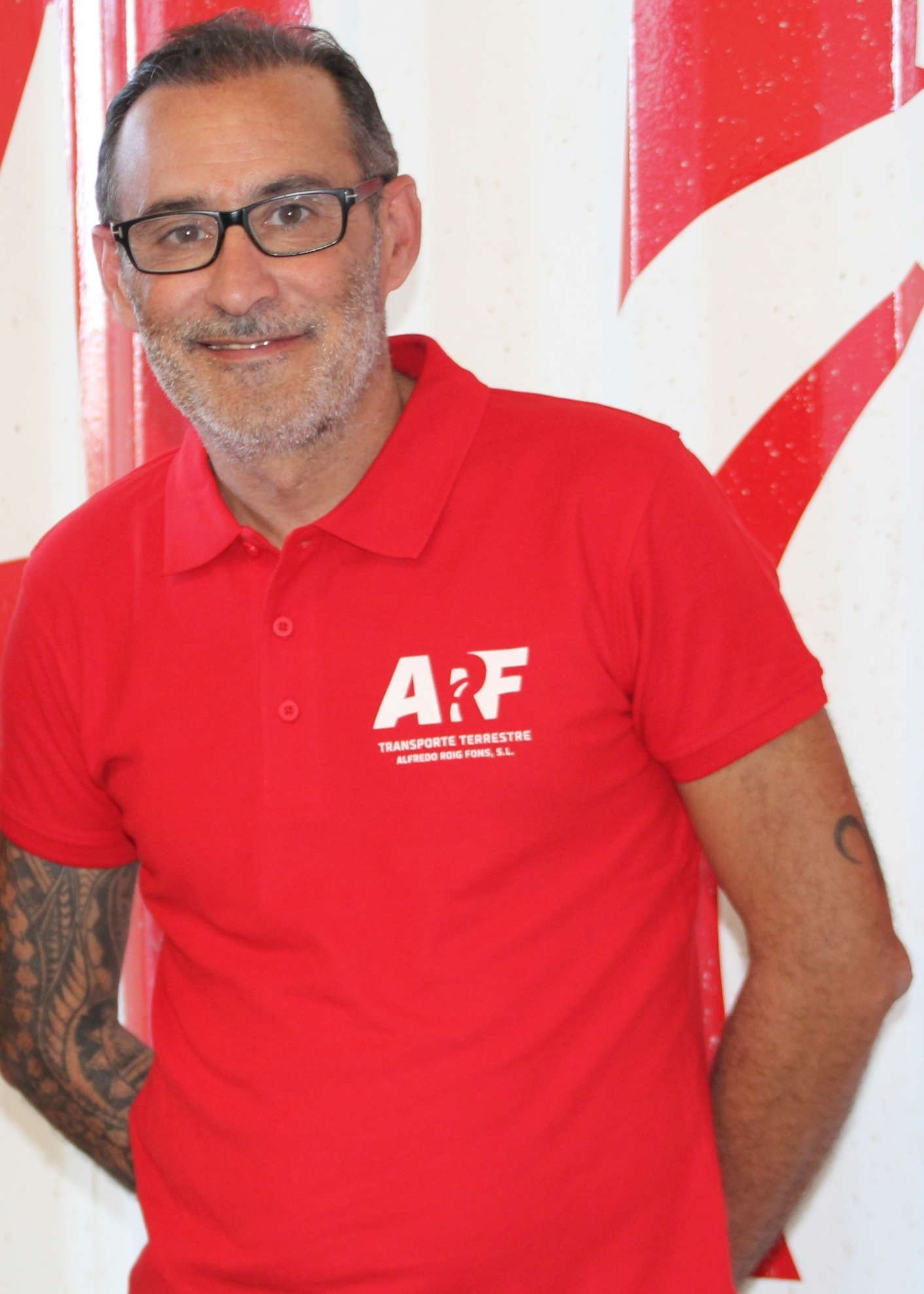Hombre con gafas sonríe, vistiendo un polo rojo con el logo 