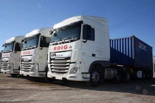 Tres camiones ROIG blancos estacionados en un día soleado, uno de ellos con un contenedor de envío azul.