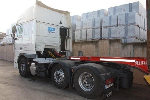 Camión semirremolque blanco con remolque rojo estacionado cerca de bloques de hormigón.