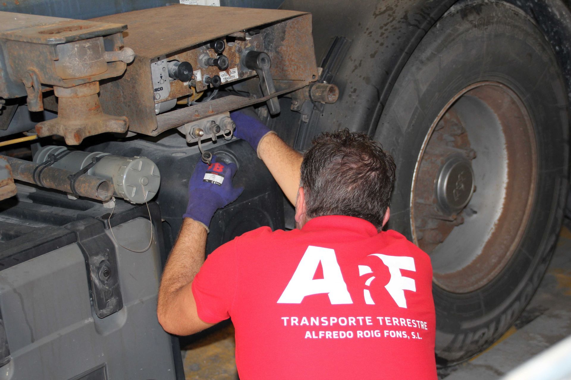 Mecánico con camisa roja y guantes, trabajando en una llanta de camión. Logotipo