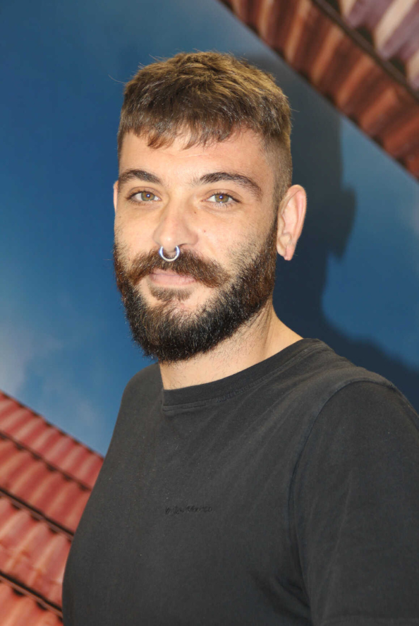 Hombre con barba y anillo en la nariz, vestido con una camisa negra, delante de un fondo azul.