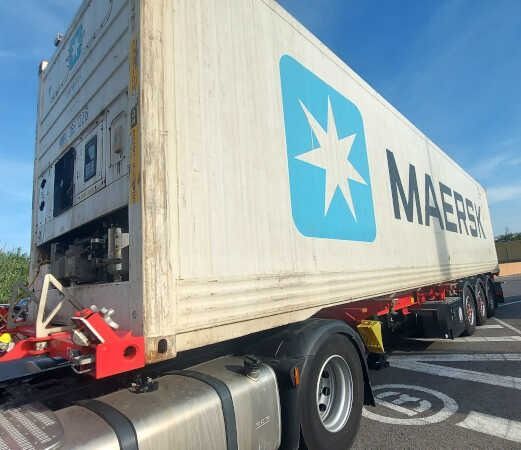 Un contenedor de envío de Maersk en un remolque de camión; colores blanco y azul.