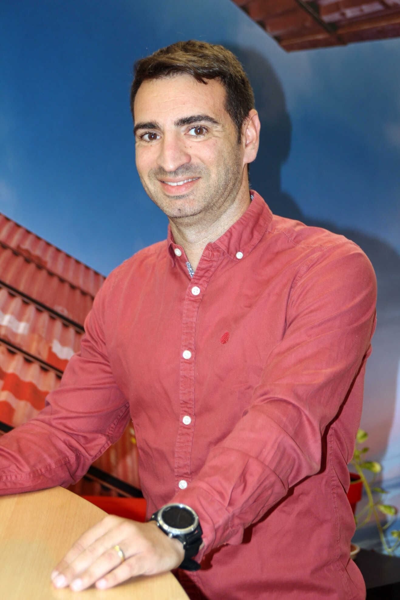 Hombre con barba y anillo en la nariz, vestido con una camisa negra, delante de un fondo azul.