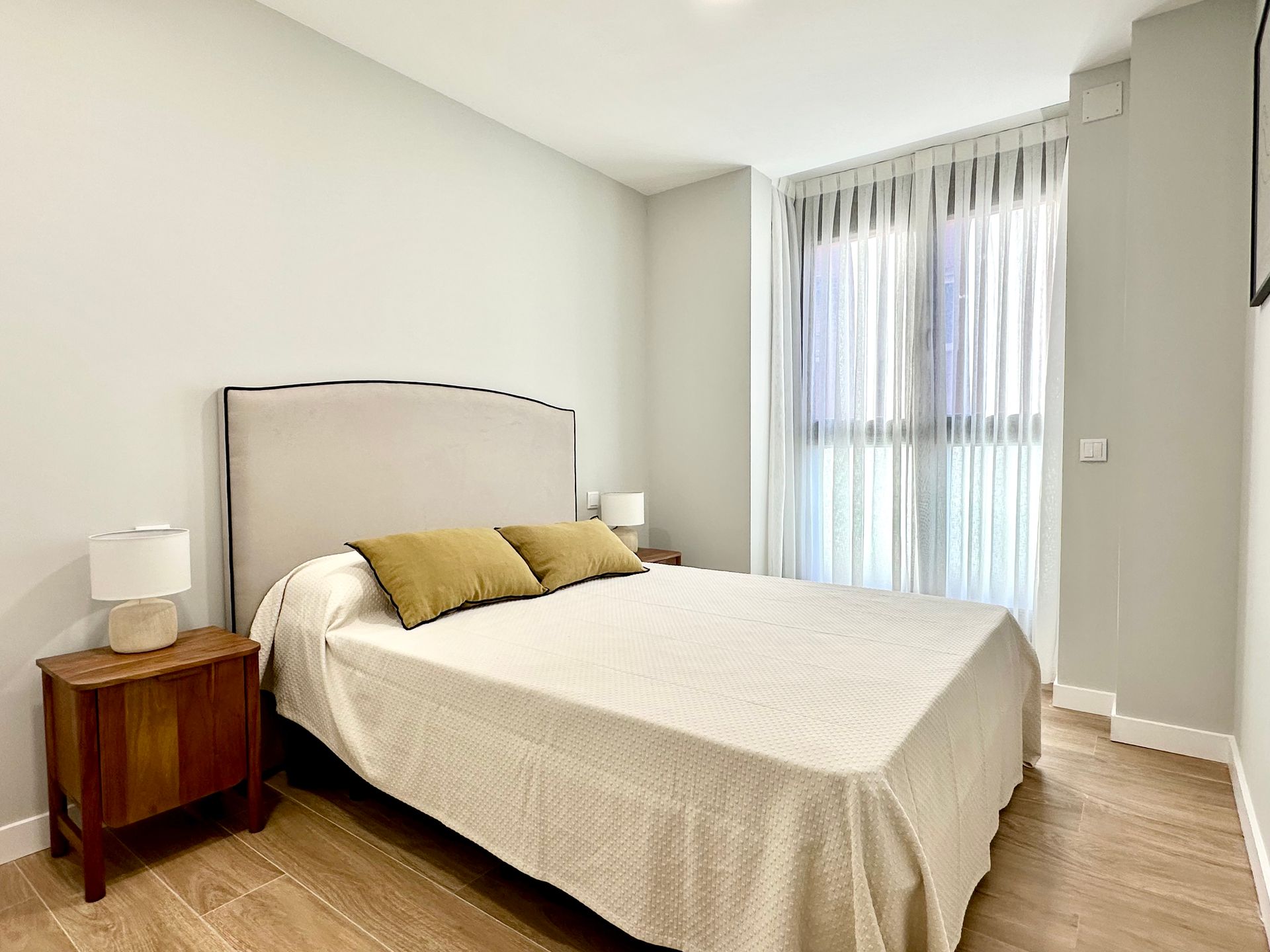 A bedroom with a bed , nightstand , lamps and a window.