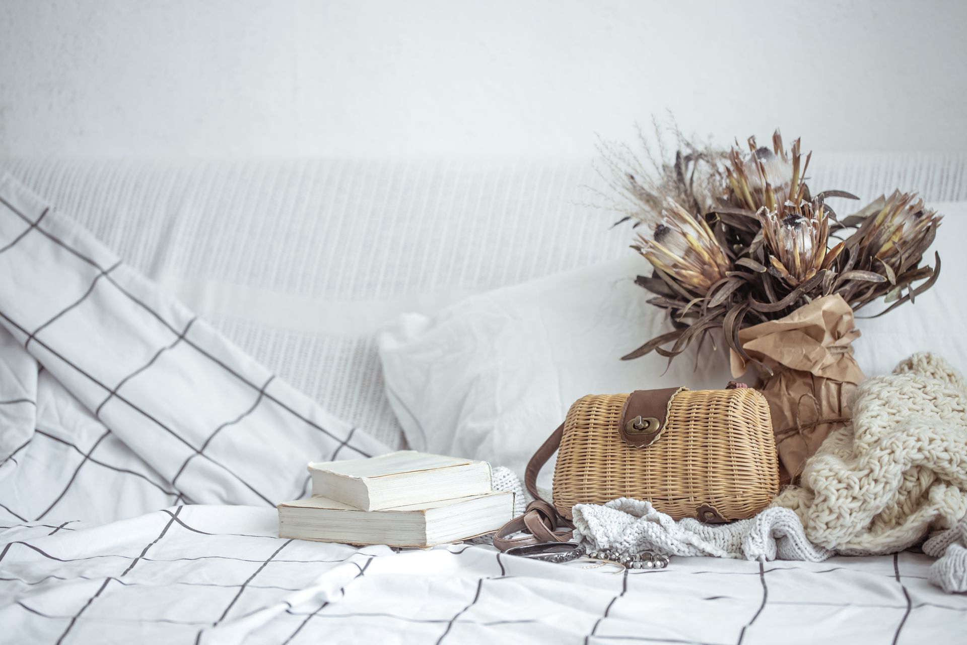 A bed with a book , purse , and flowers on it.