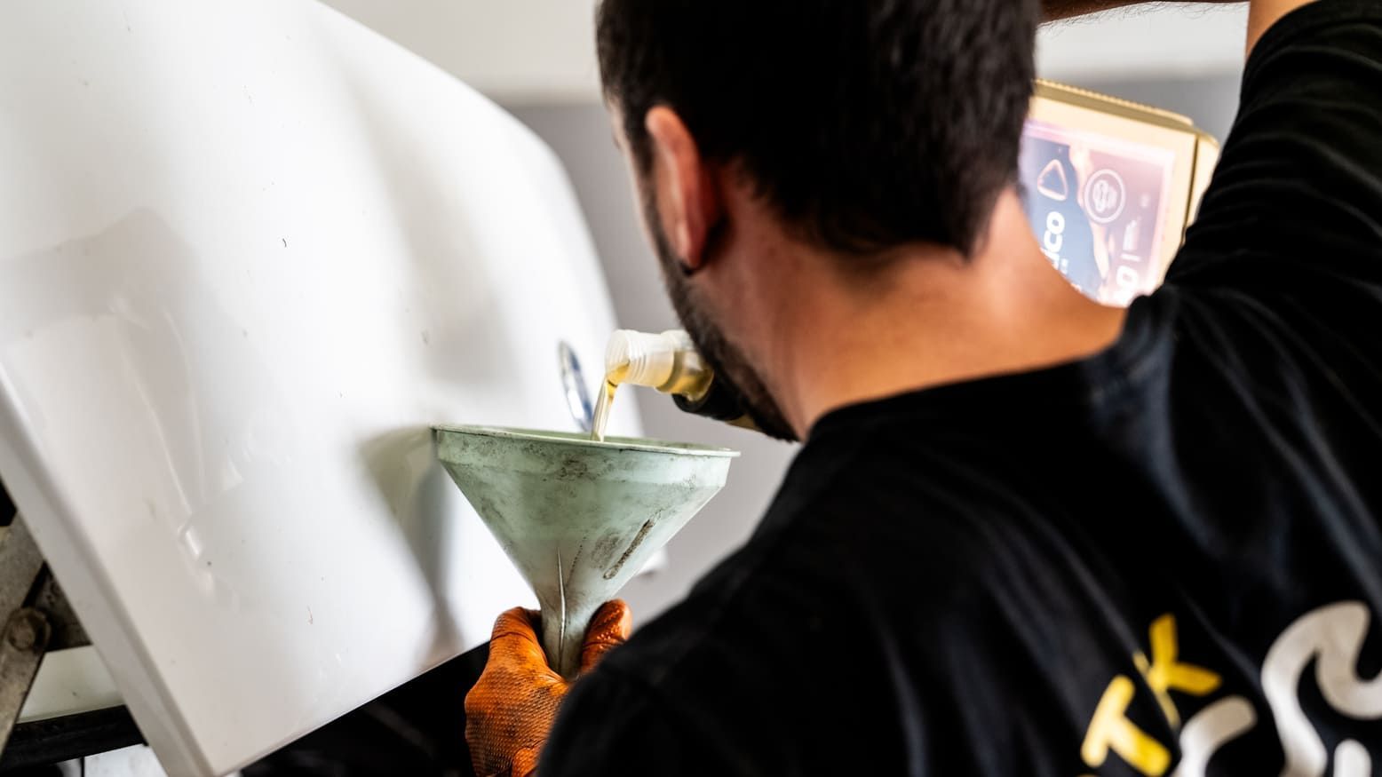 Un hombre con una camisa negra está vertiendo algo en un embudo.