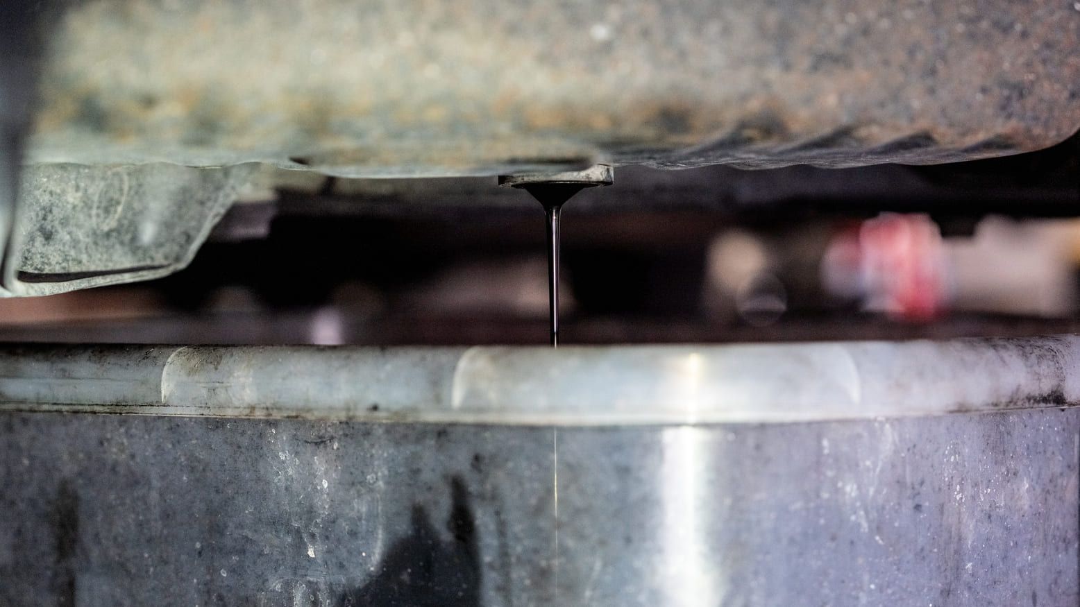 Un primer plano de un desagüe debajo de un automóvil con aceite goteando de él.